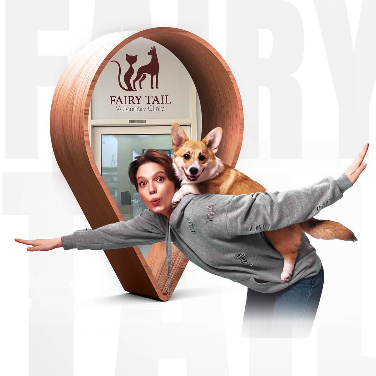 Happy corgi riding on the back of a woman posing like an airplane in front of the Fairy Tail Veterinary Clinic sign in Al Furjan